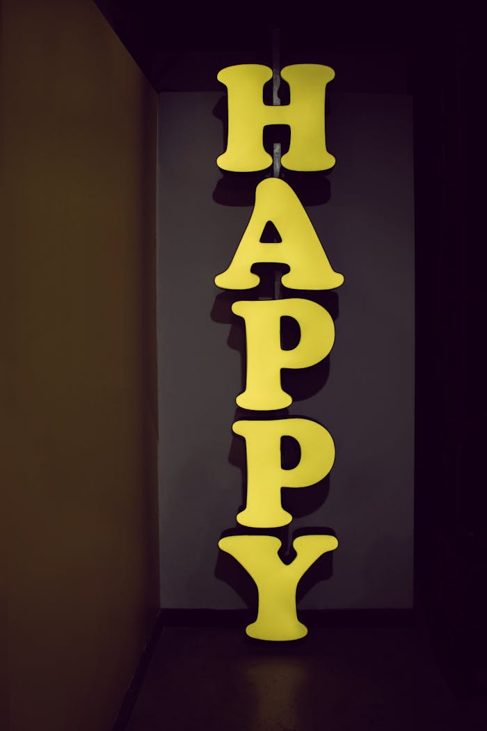Illuminated yellow 'HAPPY' sign displayed vertically in a dimly lit hallway setting, evoking a playful mood.